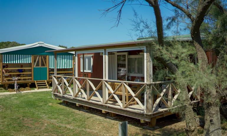 Wooden bungalow with a porch in a sunny campsite.