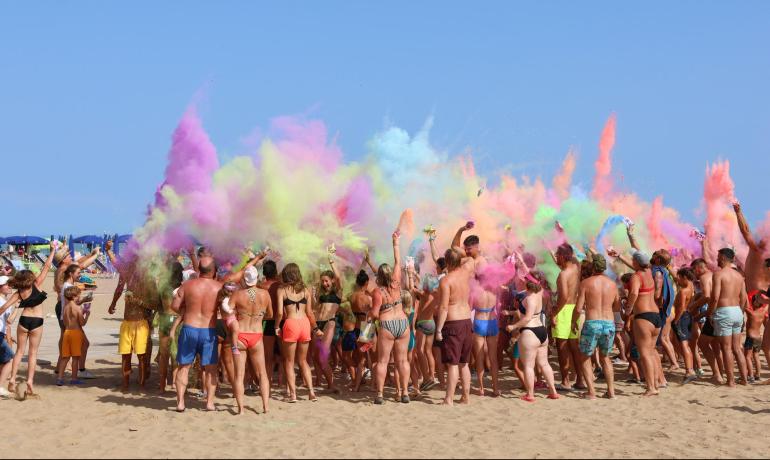 Menschen am Strand werfen bunte Pulver bei einem Fest.