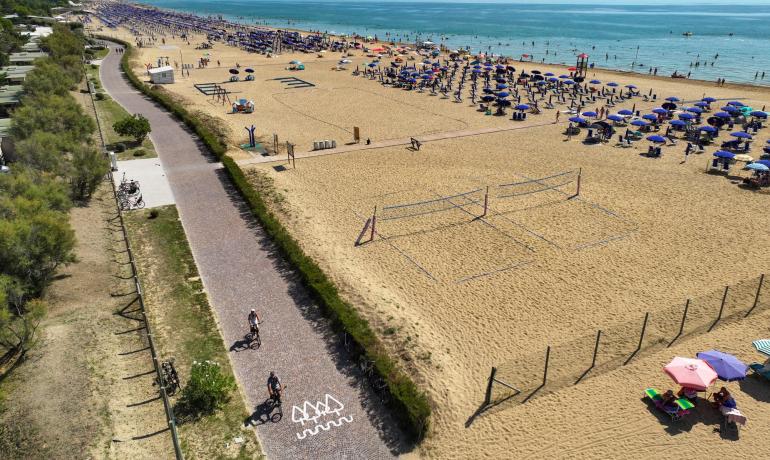 Überfüllter Strand mit Sonnenschirmen und Radweg.