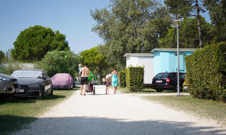 Familie spaziert im Campingplatz, geparkte Autos, bunte Bungalows.