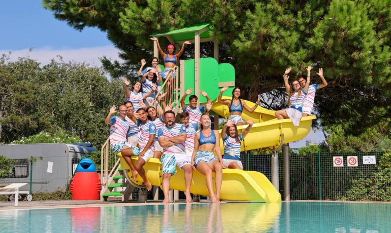 Group of smiling people on a pool slide, wearing colorful outfits.
