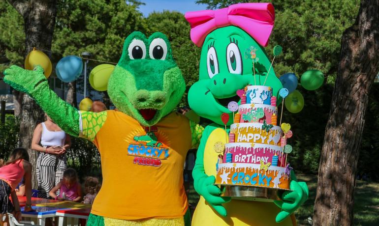 Two crocodile mascots celebrate with a colorful birthday cake.