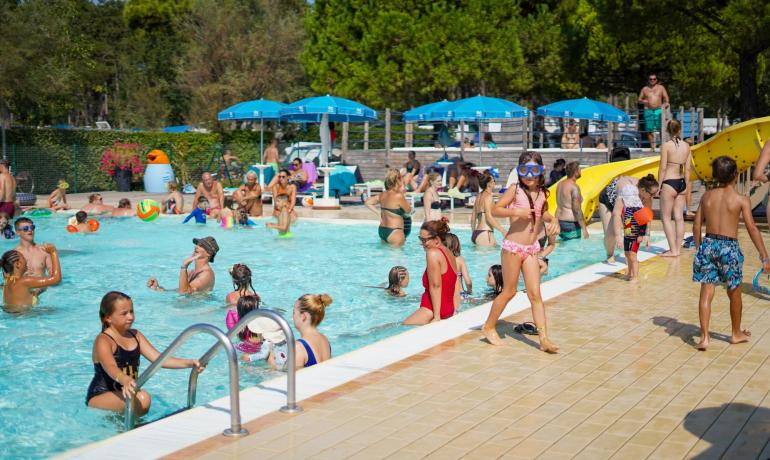 Crowded pool with kids playing and adults relaxing.