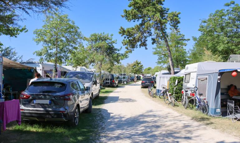 Campingplatz mit Autos, Wohnwagen und Fahrrädern entlang eines Schotterwegs.