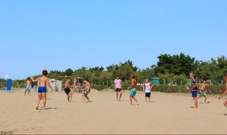Kinder spielen Volleyball am Strand unter blauem Himmel.
