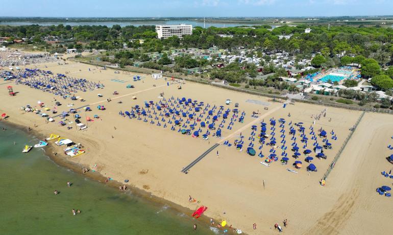 Sandstrand mit blauen Sonnenschirmen und Schwimmern, Luftaufnahme.