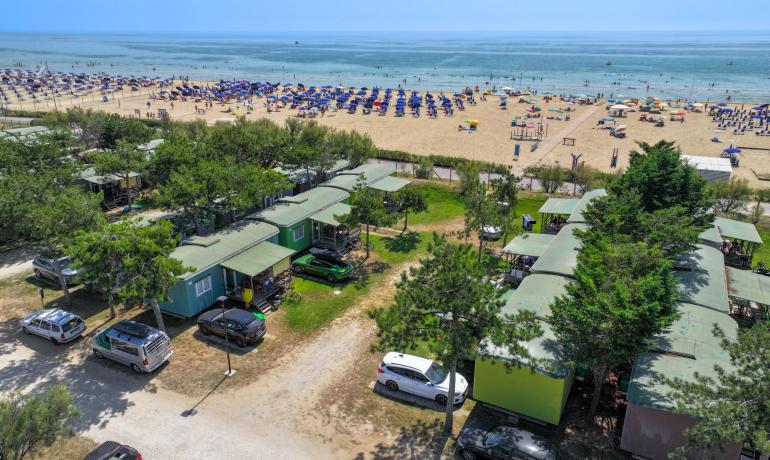 Beach with umbrellas, mobile homes, and parked cars near the sea.