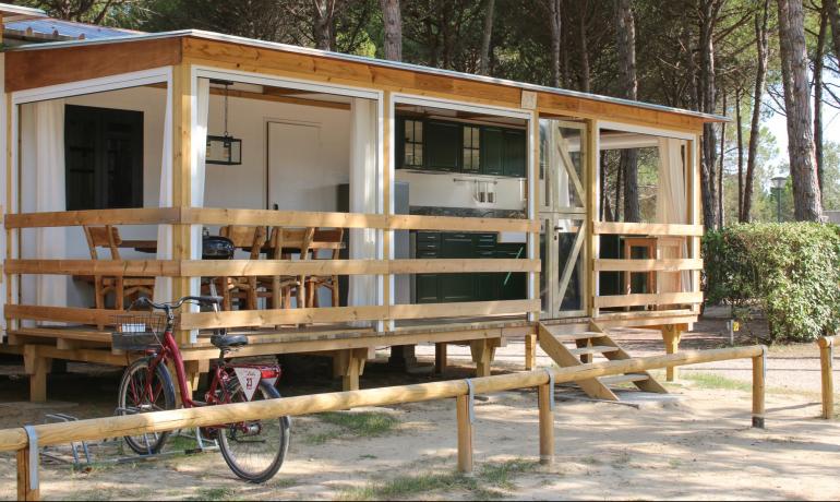 Holzbungalow mit Veranda und Fahrrad, umgeben von Natur.