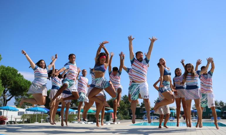 Gruppe von Menschen springt am Pool in bunten Outfits.