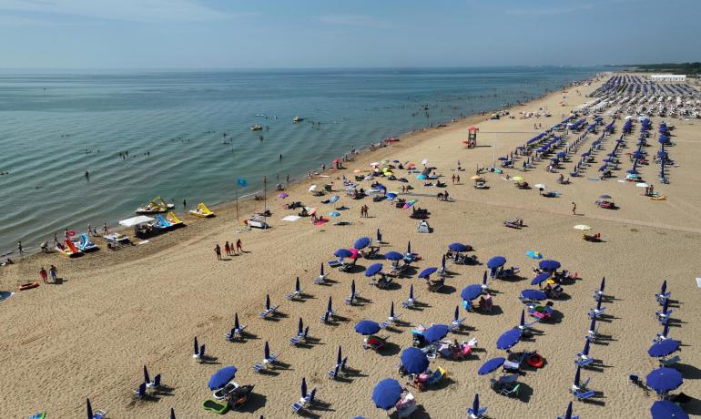Crowded beach with blue umbrellas and calm sea.