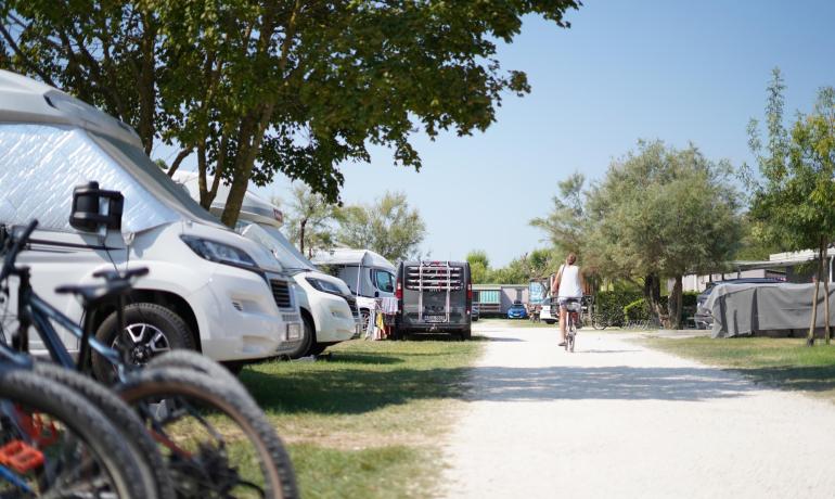 Campingplatz mit Wohnmobilen, Fahrrädern und einer radelnden Person.